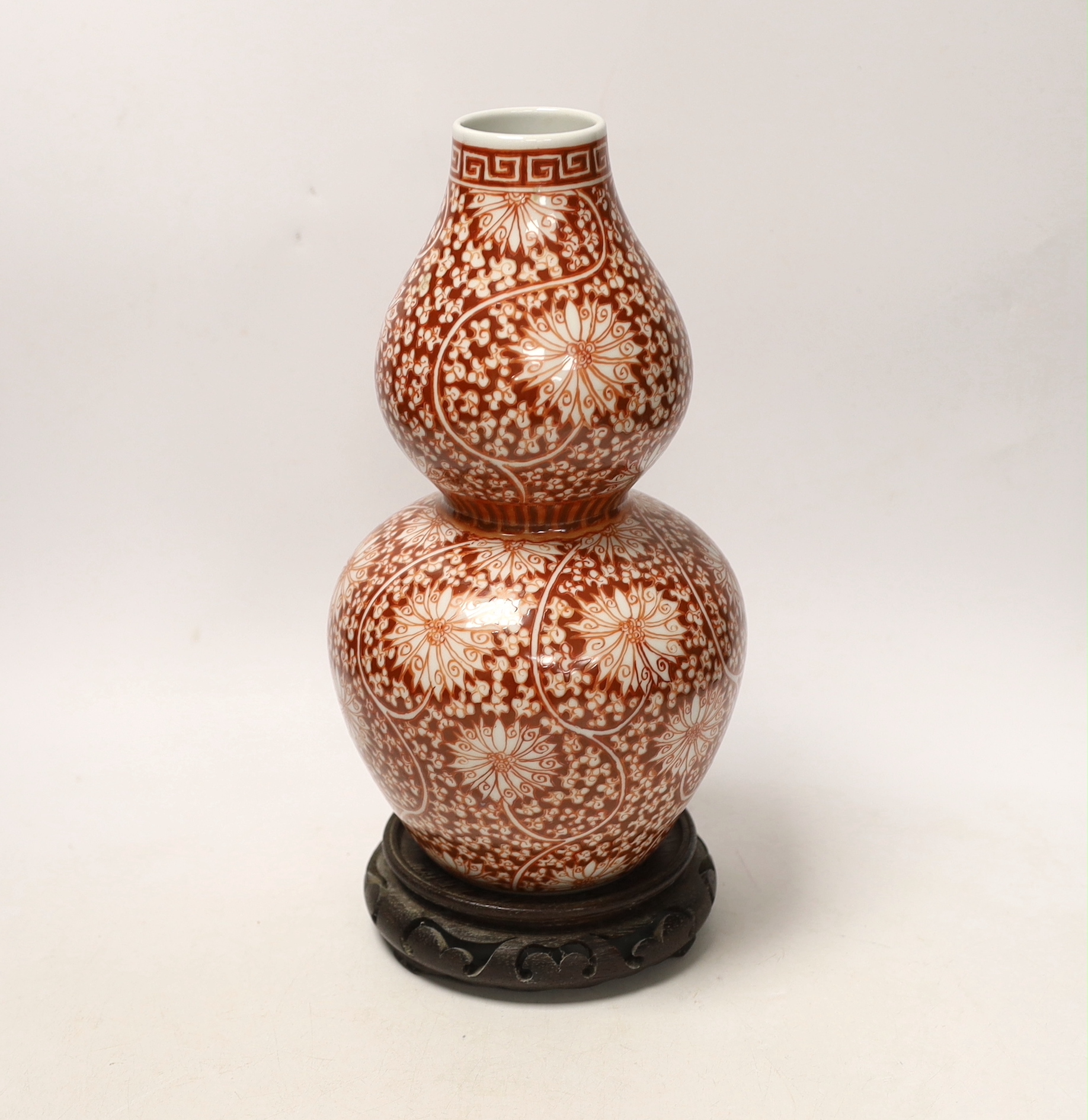 A Chinese iron-red double-gourd vase on hardwood stand, 29cm high